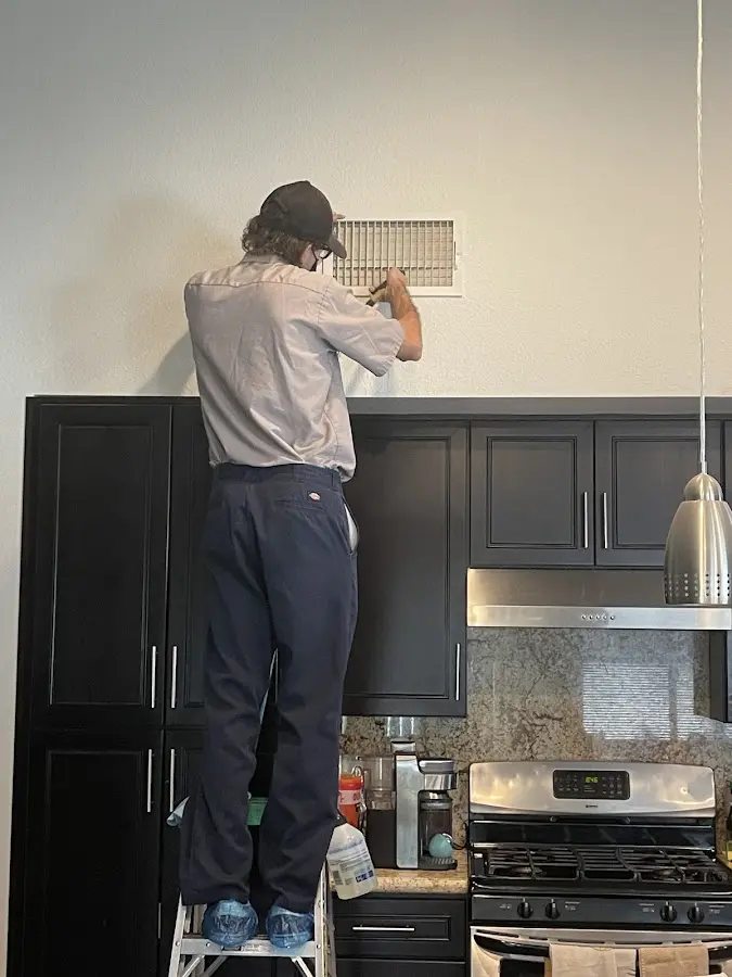 Technician inspecting an air vent during HVAC service in Warr Acres